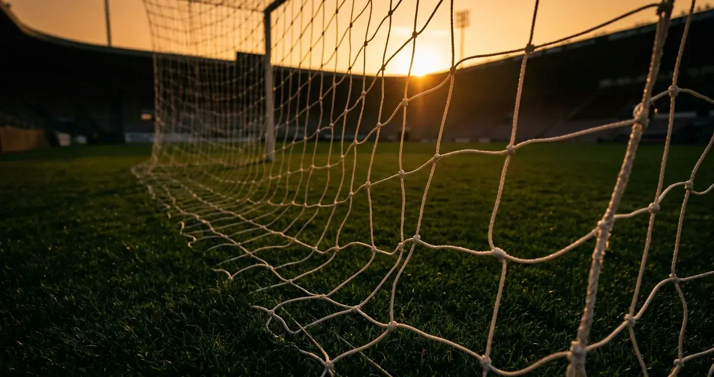 Fodboldmål med net i modlys på en tom bane ved solnedgang